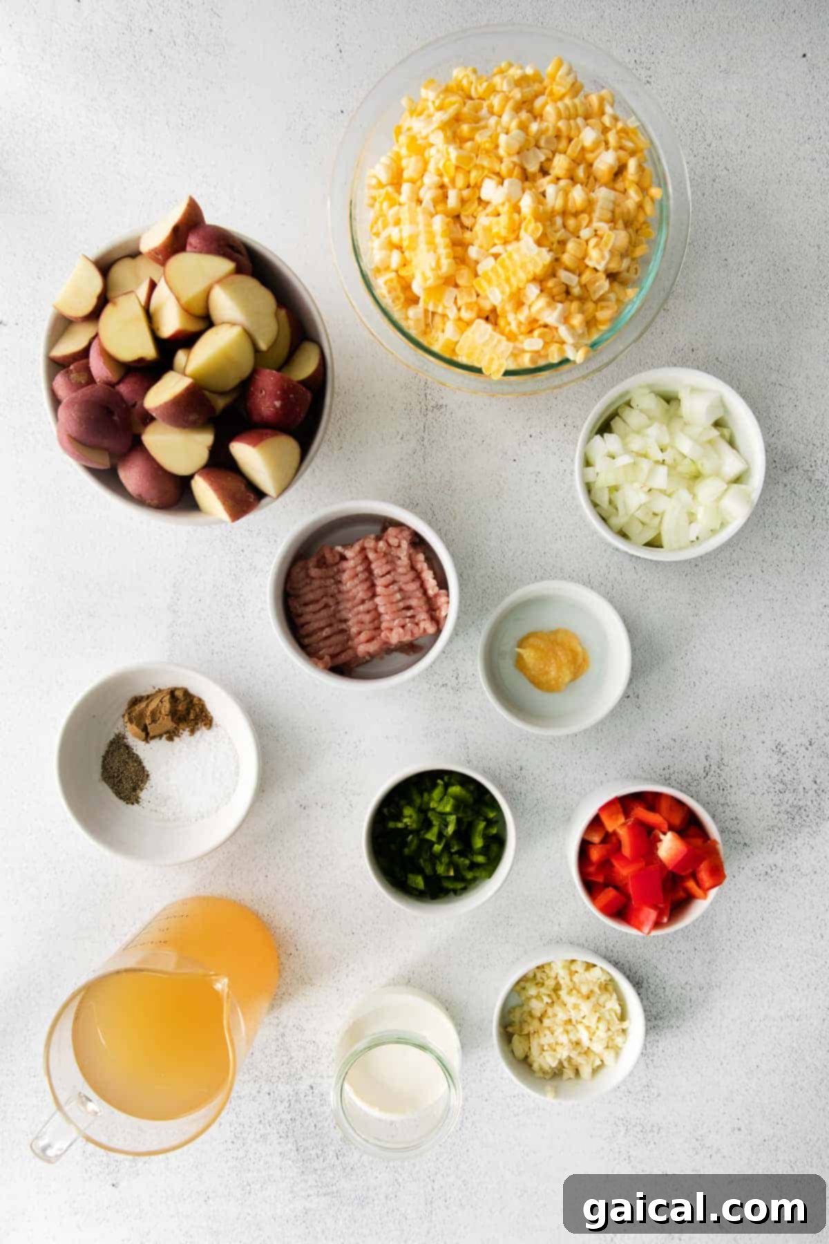 Key Ingredients for the Best Corn Chowder A rustic kitchen counter displaying a variety of fresh ingredients including ears of sweet corn, red potatoes, minced garlic, onions, ground pork, and spices, ready for making corn chowder.