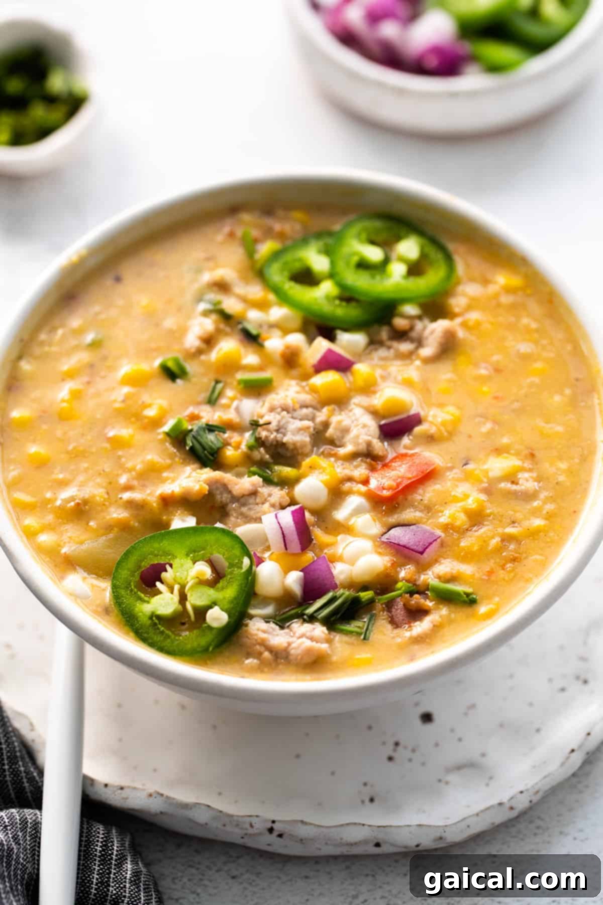 Garnished Sweet Corn Chowder A vibrant bowl of corn chowder, generously garnished with crispy ground pork, fresh chives, and a sprinkle of red pepper flakes.