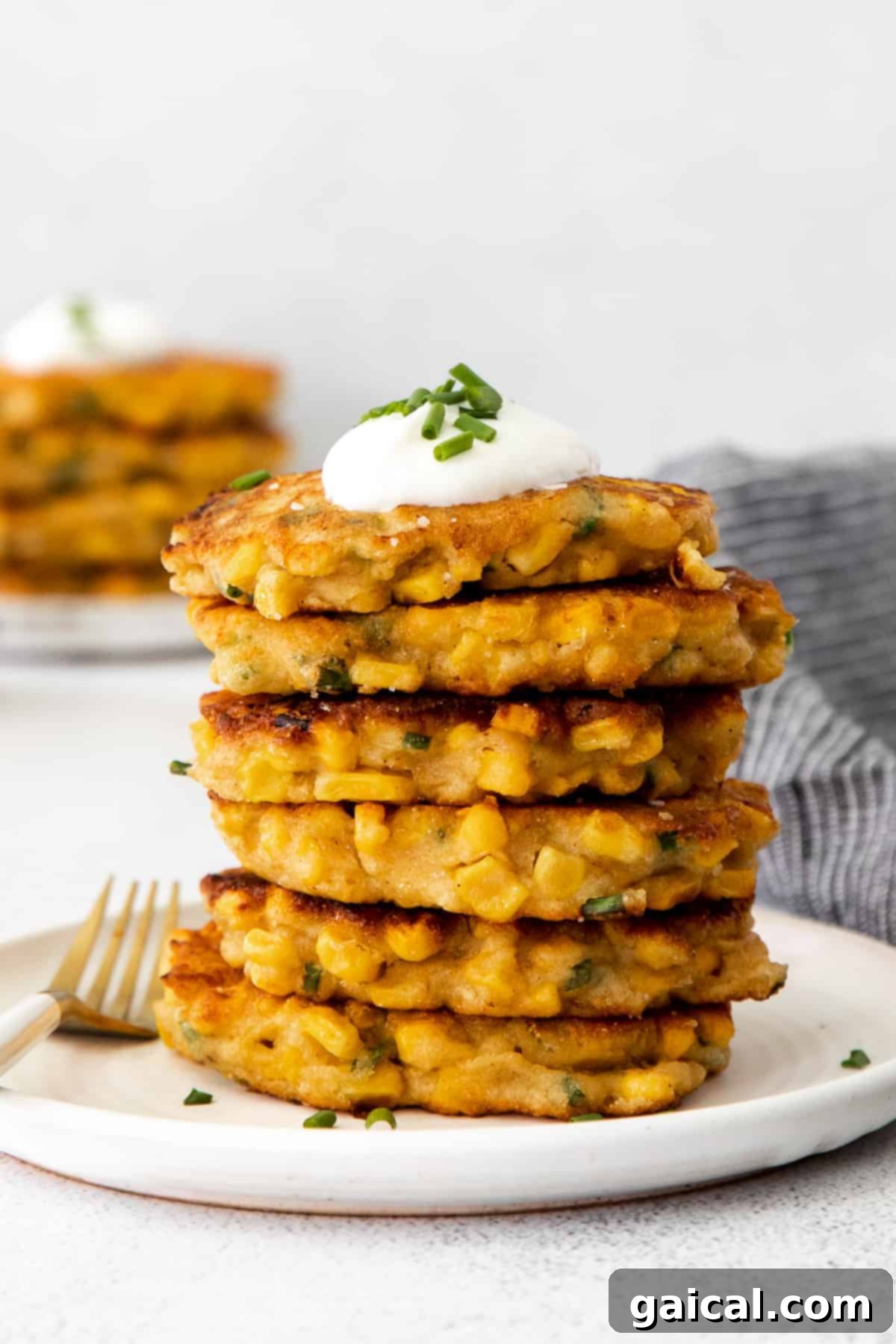 A stack of golden brown corn fritters generously topped with creamy Greek yogurt and freshly chopped chives, presented invitingly.