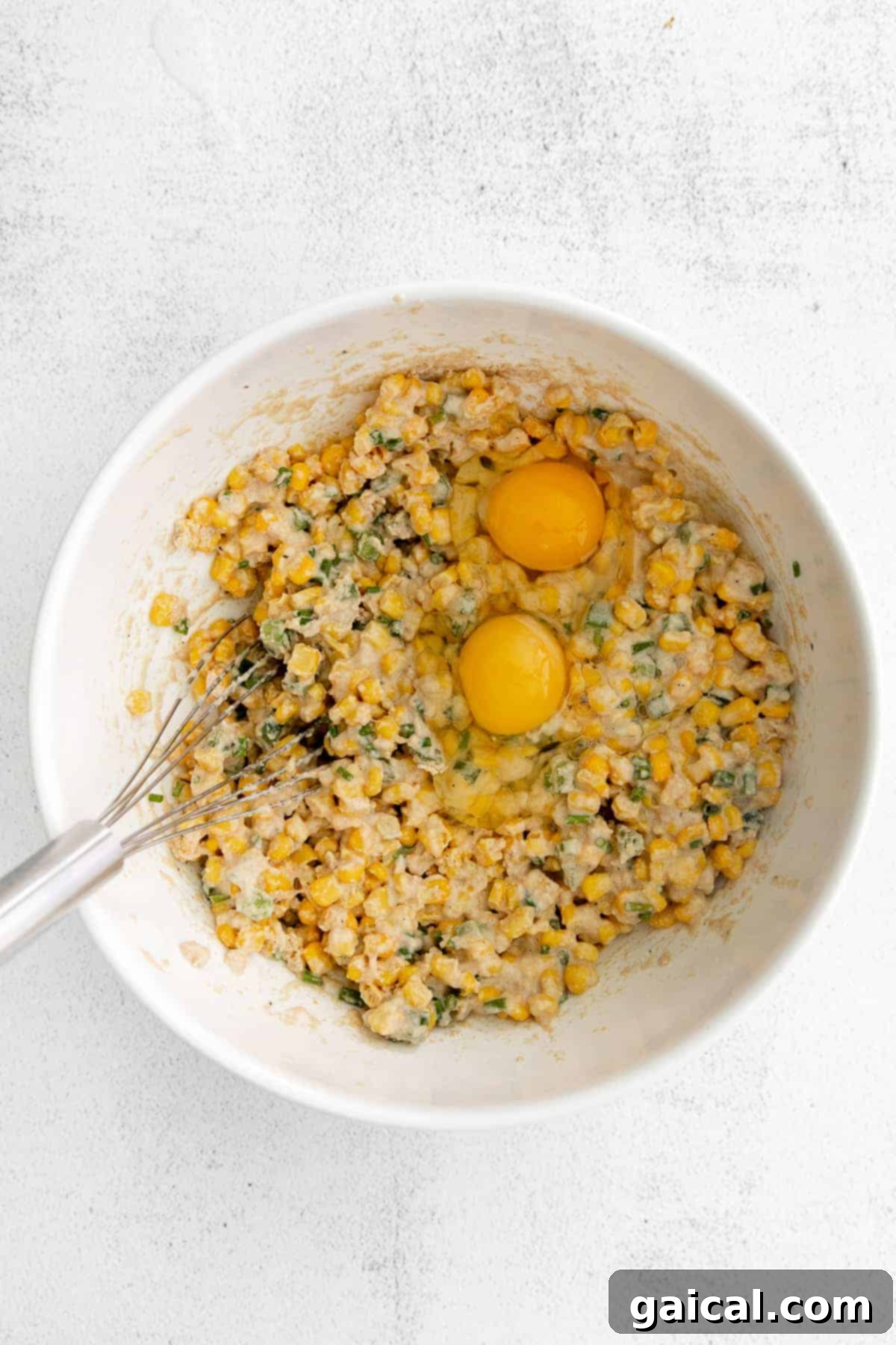 Close-up shot of corn fritter batter with whole eggs cracked over it, ready to be mixed for a delicious meal.