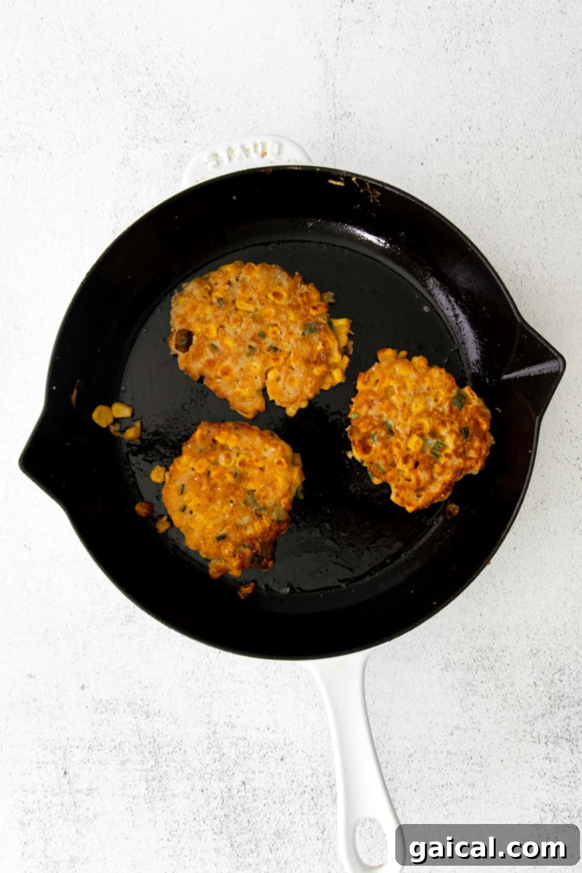 Several perfectly crispy corn fritters sizzling in a hot cast iron pan, achieving a beautiful golden-brown color.