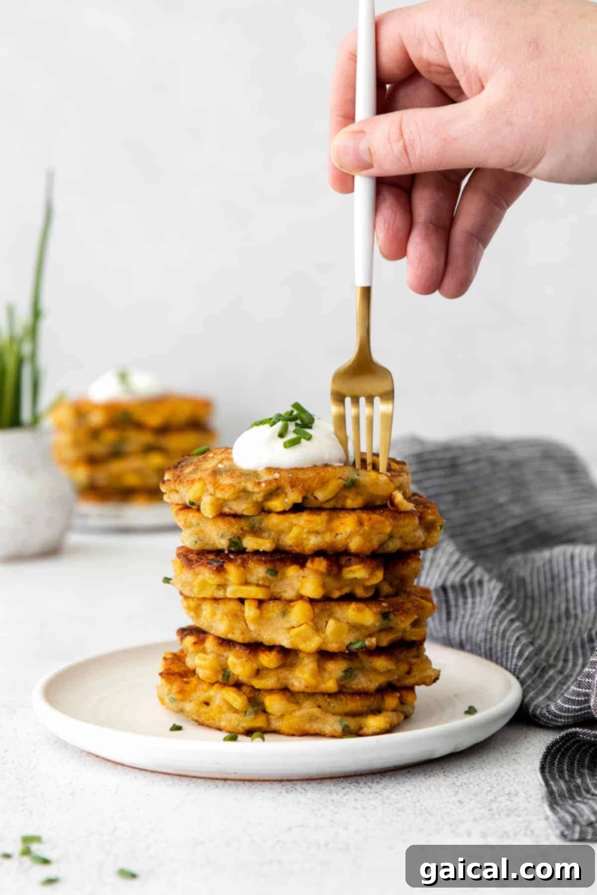 A beautifully arranged stack of golden corn fritters, elegantly garnished with a dollop of creamy Greek yogurt and a sprinkle of fresh chives.