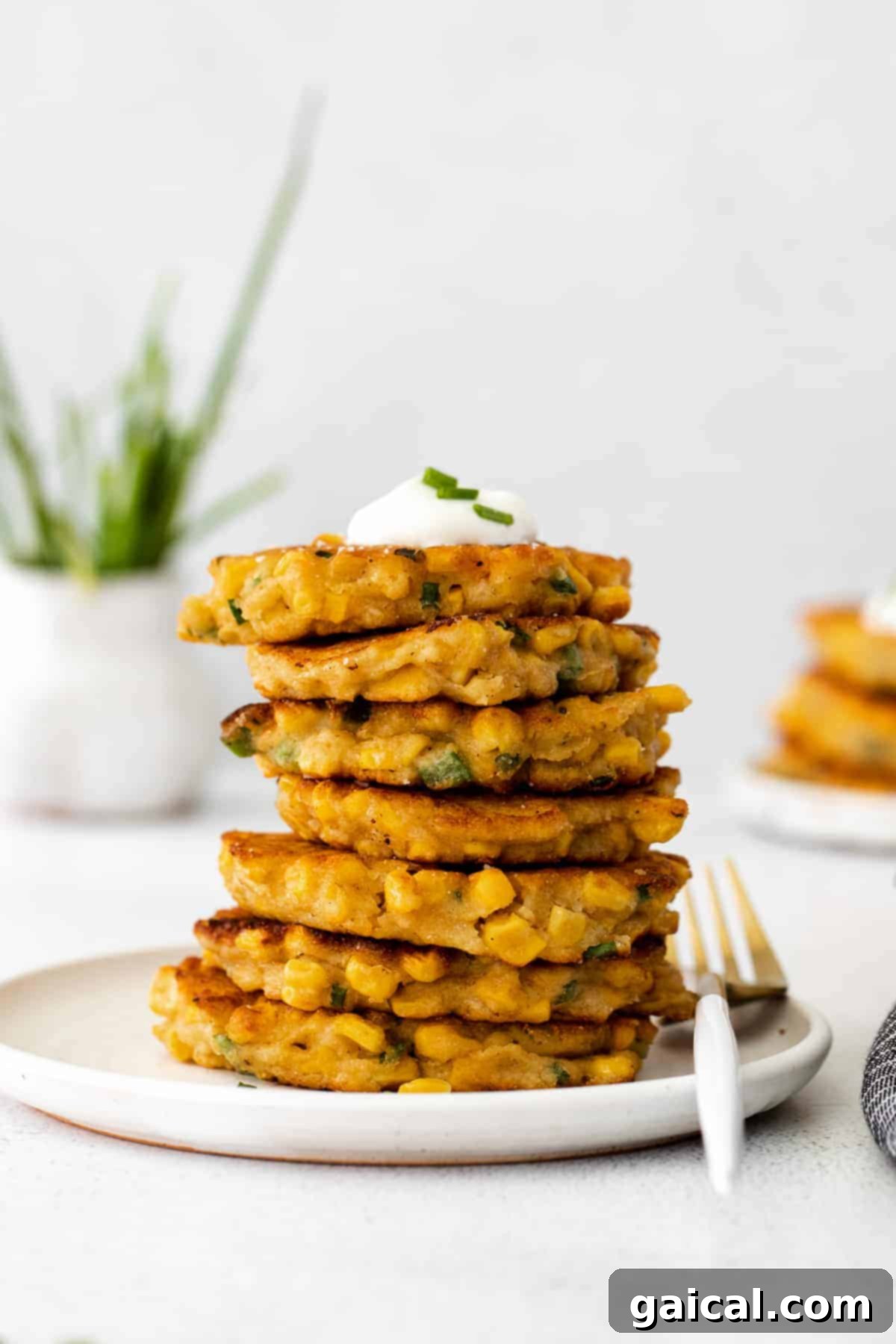 Close-up of crispy corn fritters topped with a generous dollop of Greek yogurt, highlighting their texture and fresh garnishes.