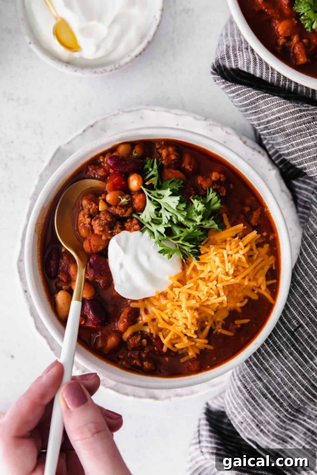 A steaming bowl of Instant Pot chili, generously topped with shredded cheese, a dollop of Greek yogurt, and fresh parsley for garnish.
