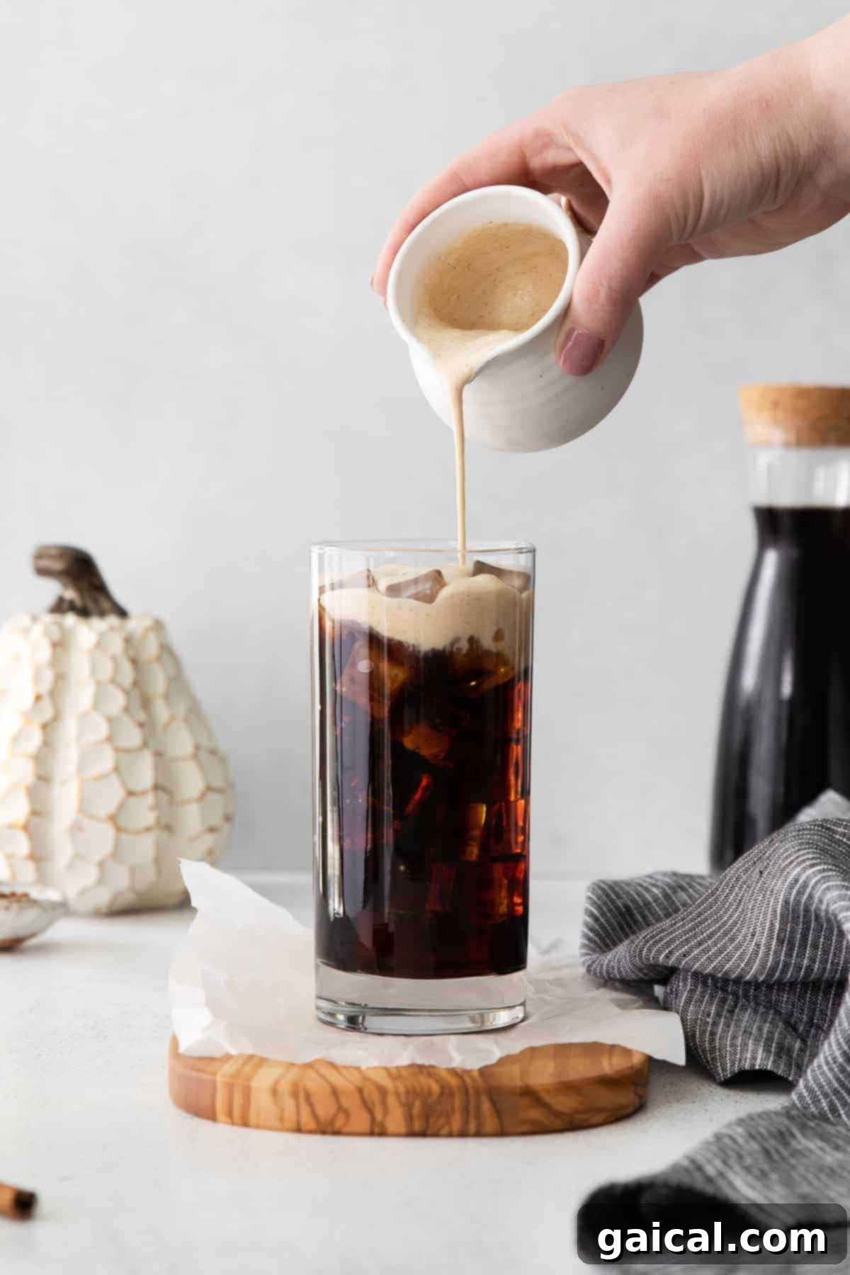 Pouring the pumpkin sweet cream over ice and cold brew in a glass.
