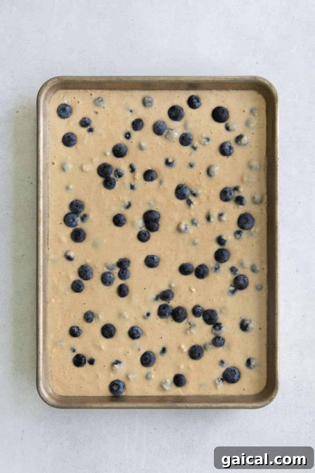 Sheet Pan Pancakes Ready for Oven Pancake batter spread evenly on a sheet pan, topped with fresh blueberries, ready to be baked into delicious sheet pan pancakes.