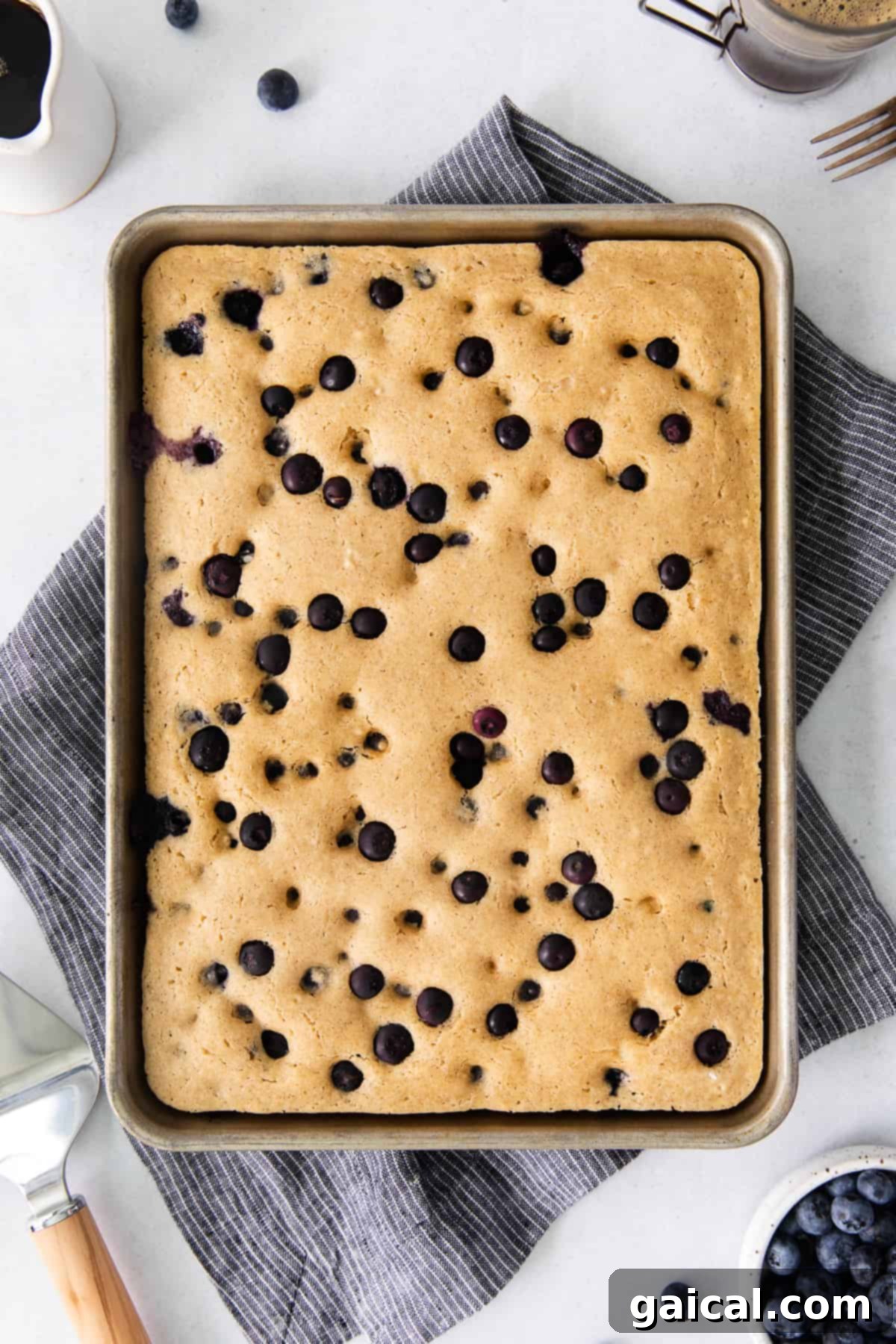Sheet Pan Pancakes Cut into Squares Freshly baked sheet pan pancakes cut into squares on a wooden cutting board, garnished with blueberries and ready to be served.
