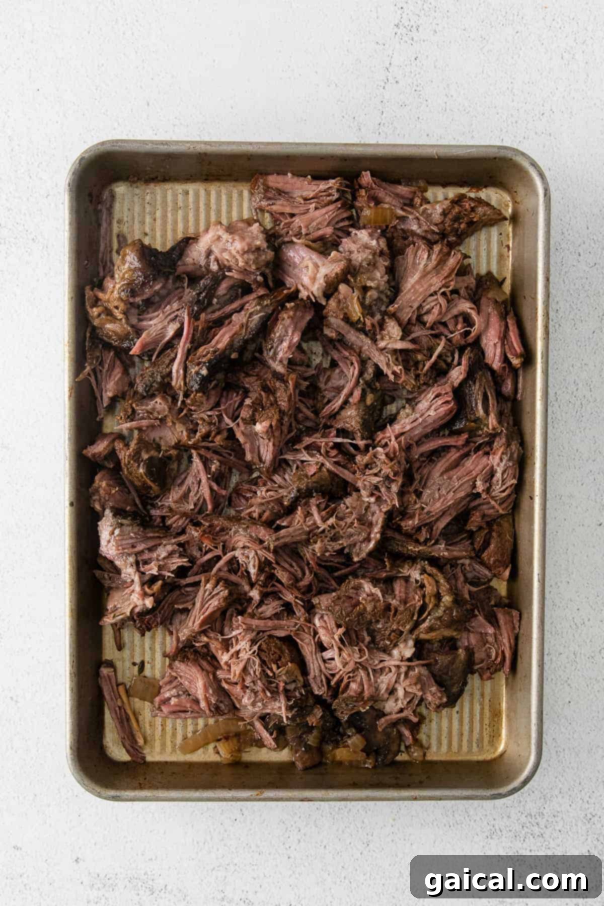 Perfectly shredded beef spread on a baking sheet, showcasing its tender texture after slow cooking.