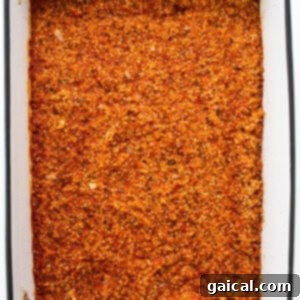 A baking dish filled with a cooking mixture of spices and quinoa, showing progress during baking.