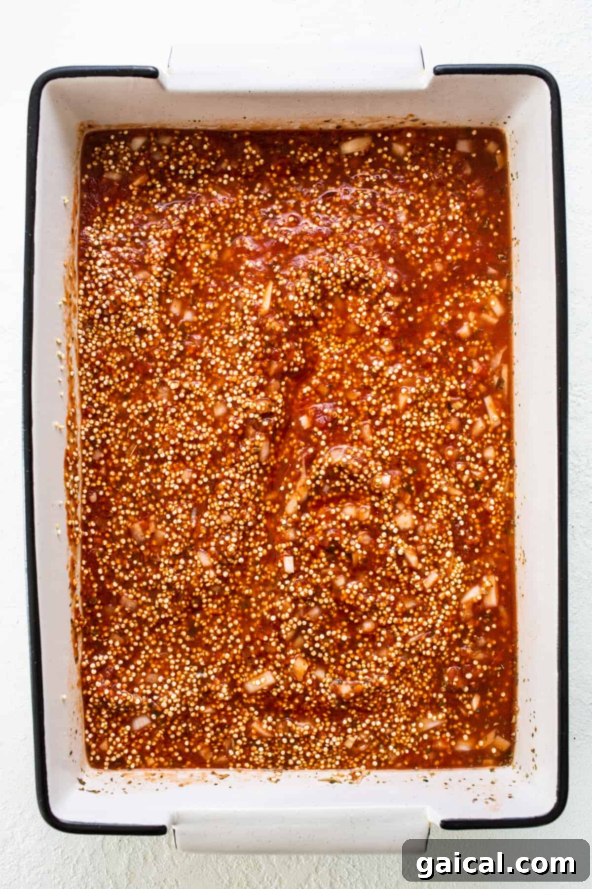 Wholesome Quinoa Pizza Bake 4 A baking dish containing a seasoned mixture of quinoa, marinara sauce, and other spices, ready for baking.
