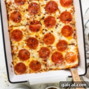 Pepperoni pizza in a baking dish with a spoon, highlighting its hearty texture.