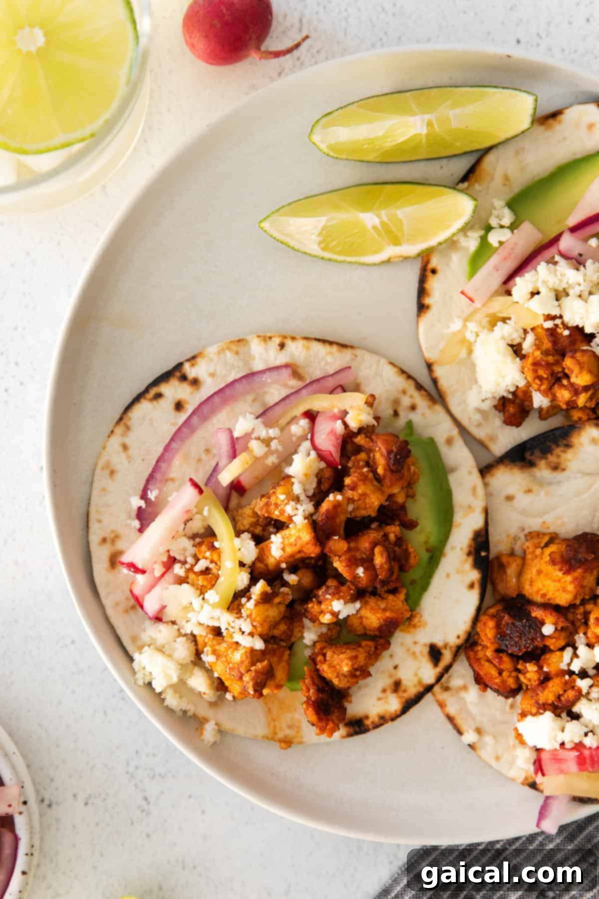 Tofu tacos on a plate, garnished with fresh cilantro and lime wedges.