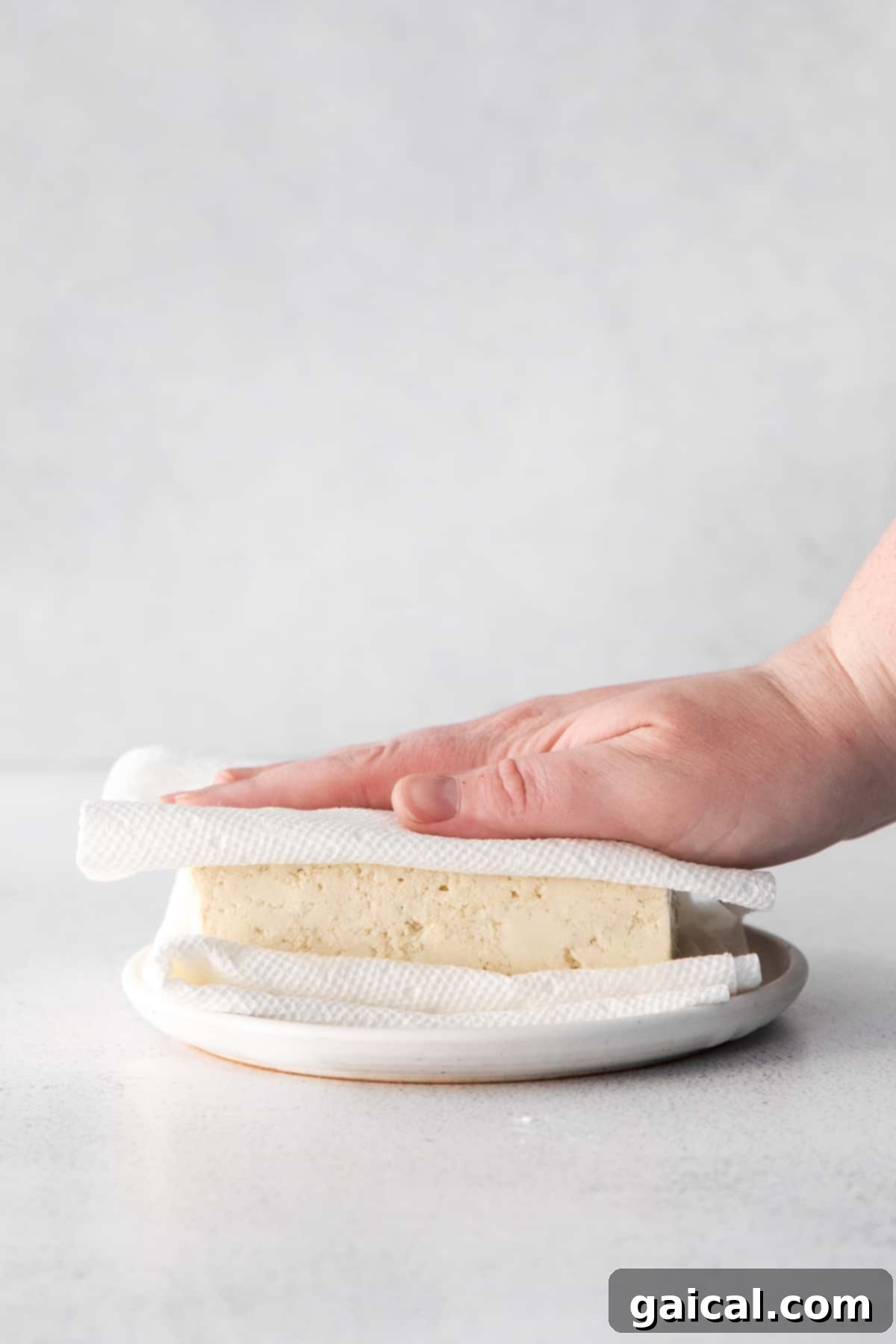 Removing excess moisture from a block of tofu using paper towels.
