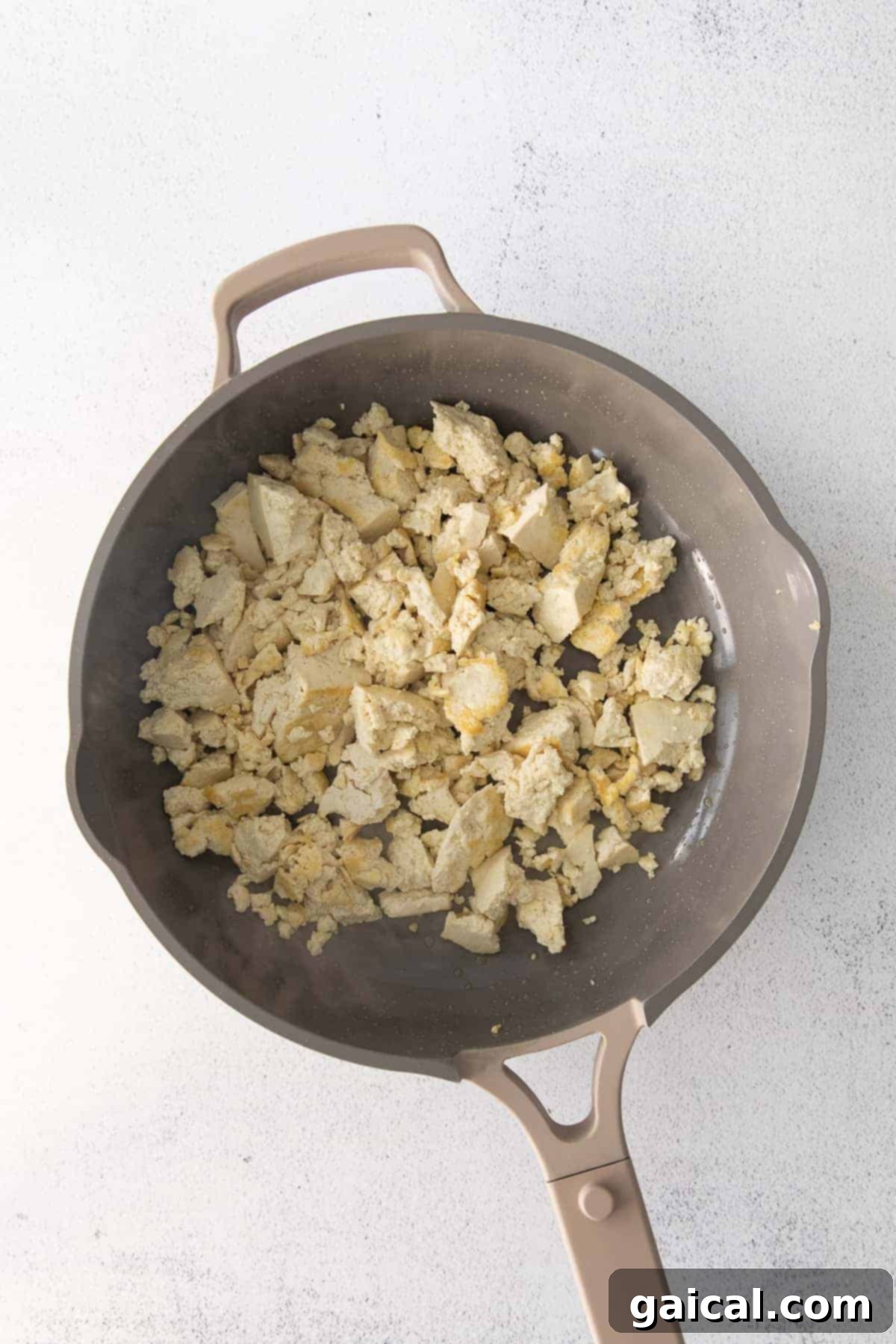 Crumbled extra-firm tofu cooking in a pan, turning golden brown.