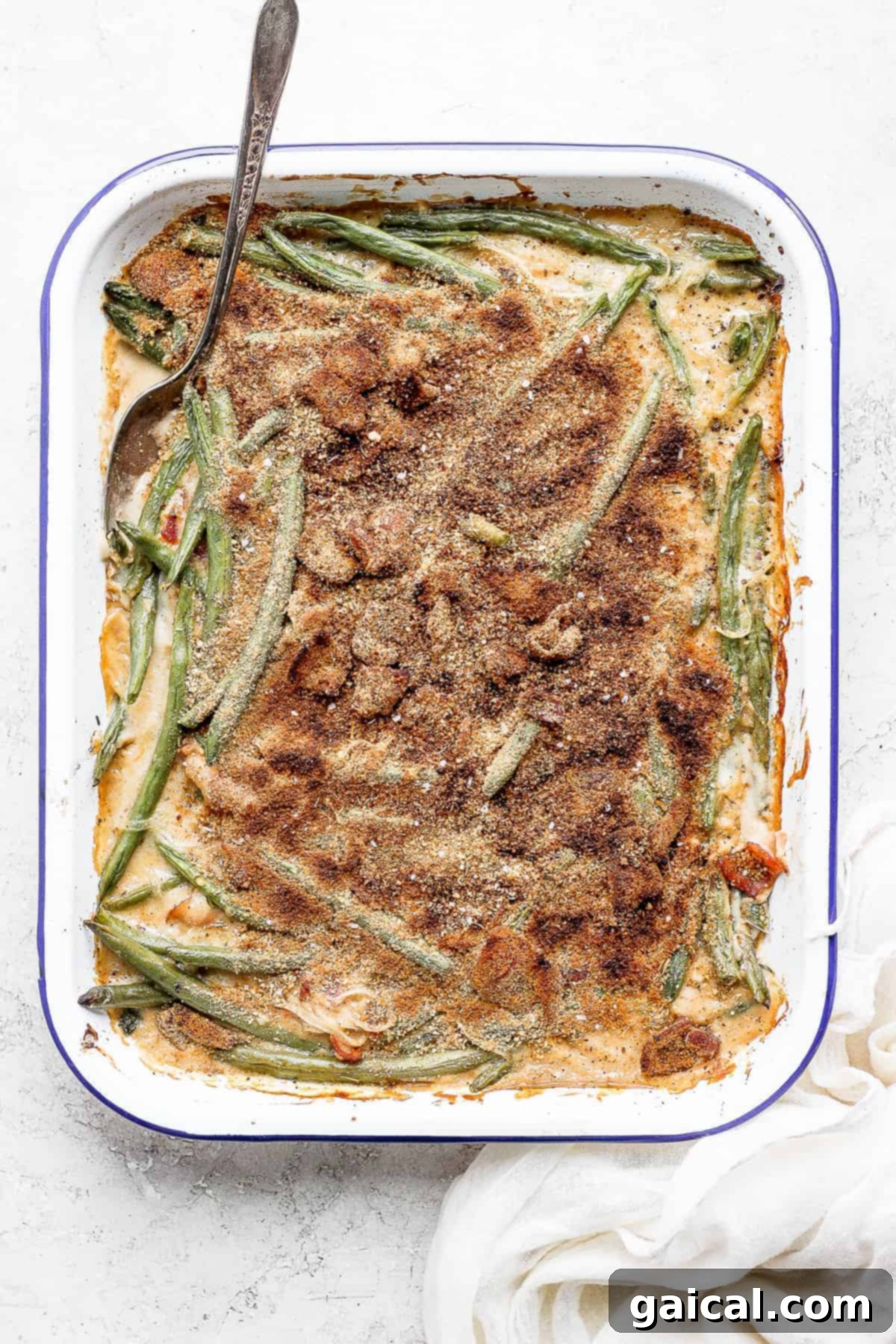 This green bean casserole with bacon is a homemade version of a classic recipe, but instead of using a cream of mushroom soup it features an amazing bacon roux. green bean casserole with bacon in a dish with a spoon