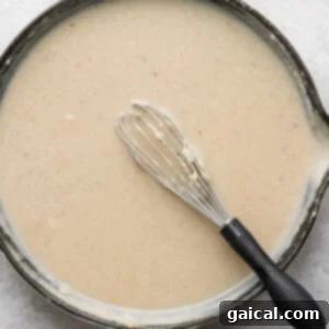 A skillet full of gravy with a whisk in it.