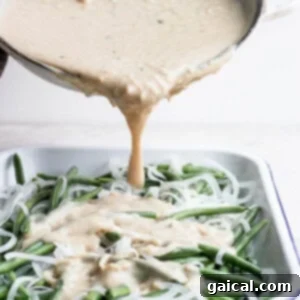 A sauce being poured over green beans in a white dish.