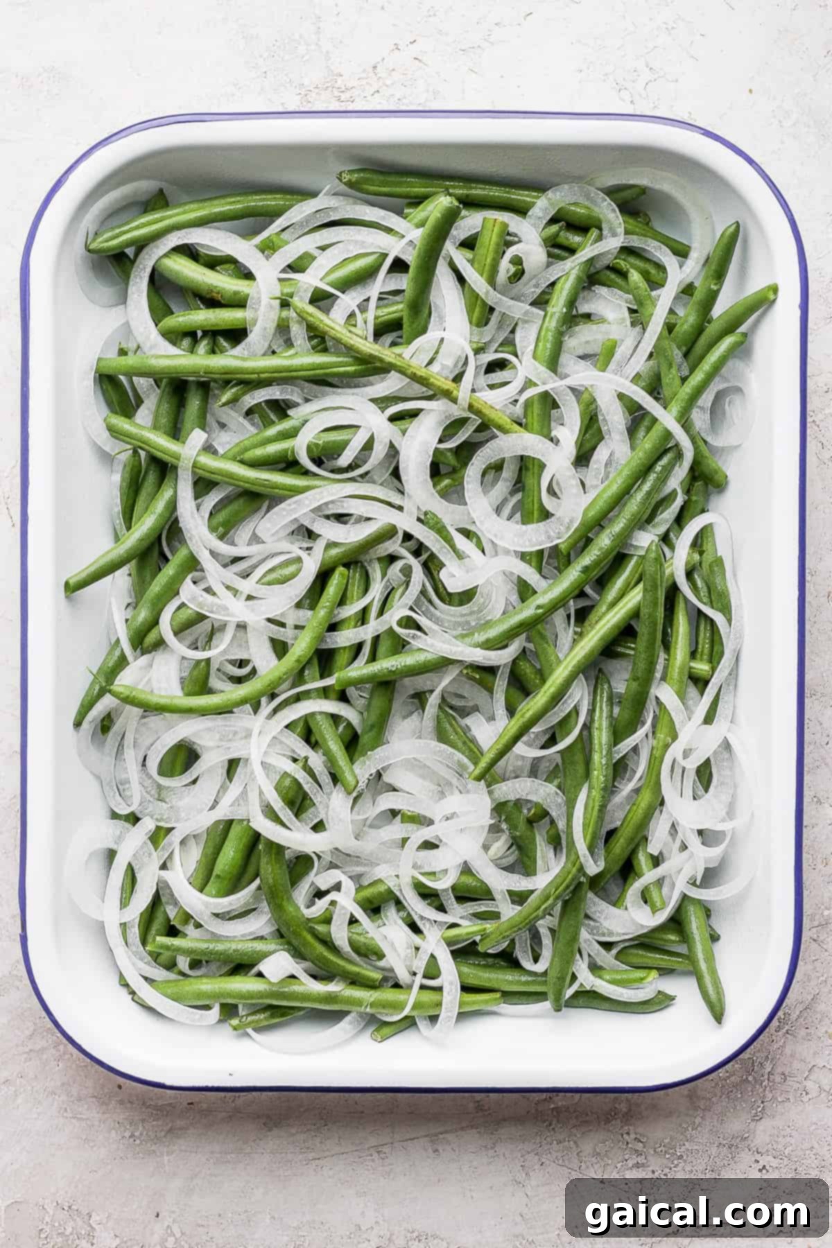 This green bean casserole with bacon is a homemade version of a classic recipe, but instead of using a cream of mushroom soup it features an amazing bacon roux. green beans and sliced onions in a casserole dish