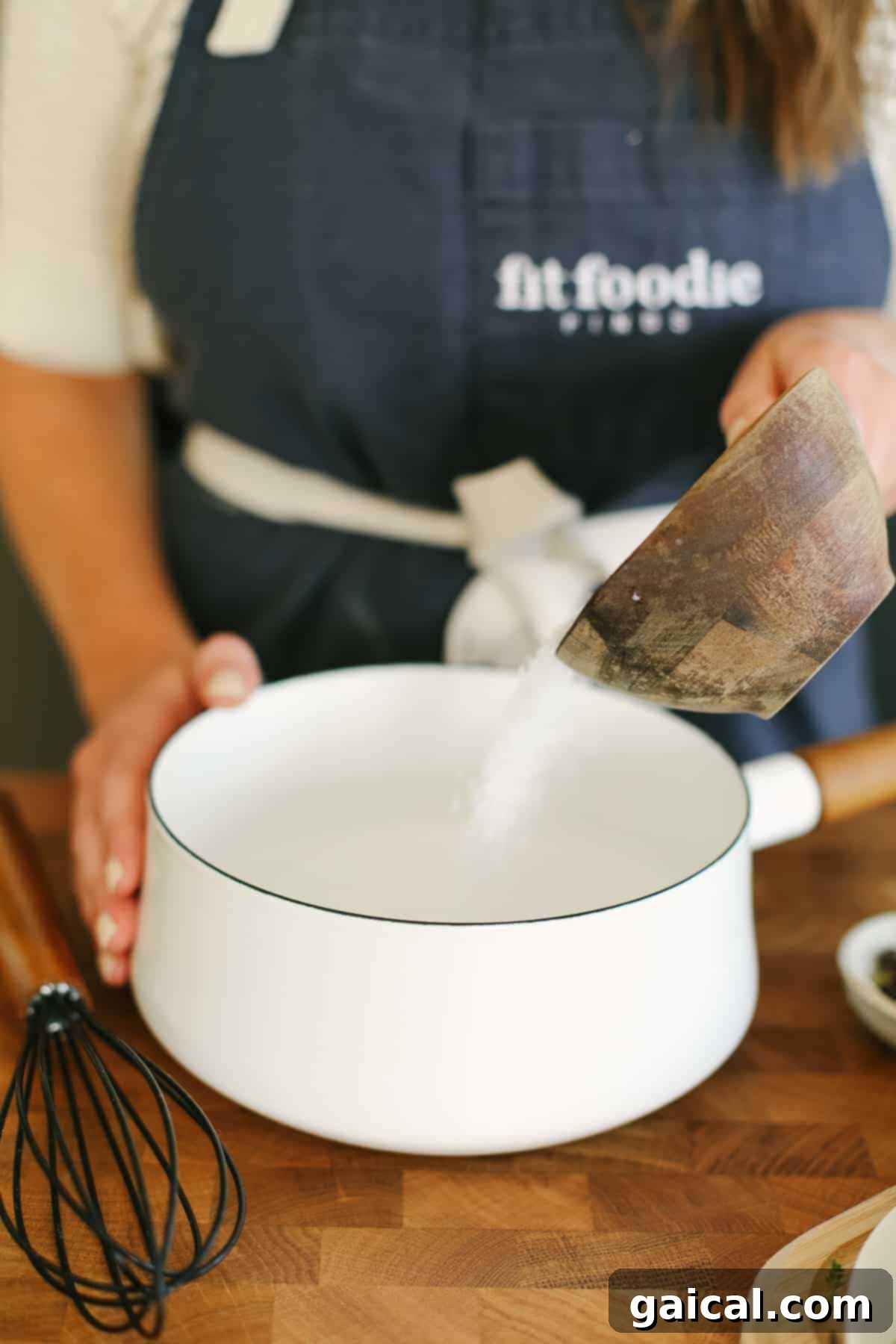 Ultimate Smoked Turkey Brine 7 A person carefully pouring kosher salt into a small saucepan of water, preparing the initial solution for the turkey brine.