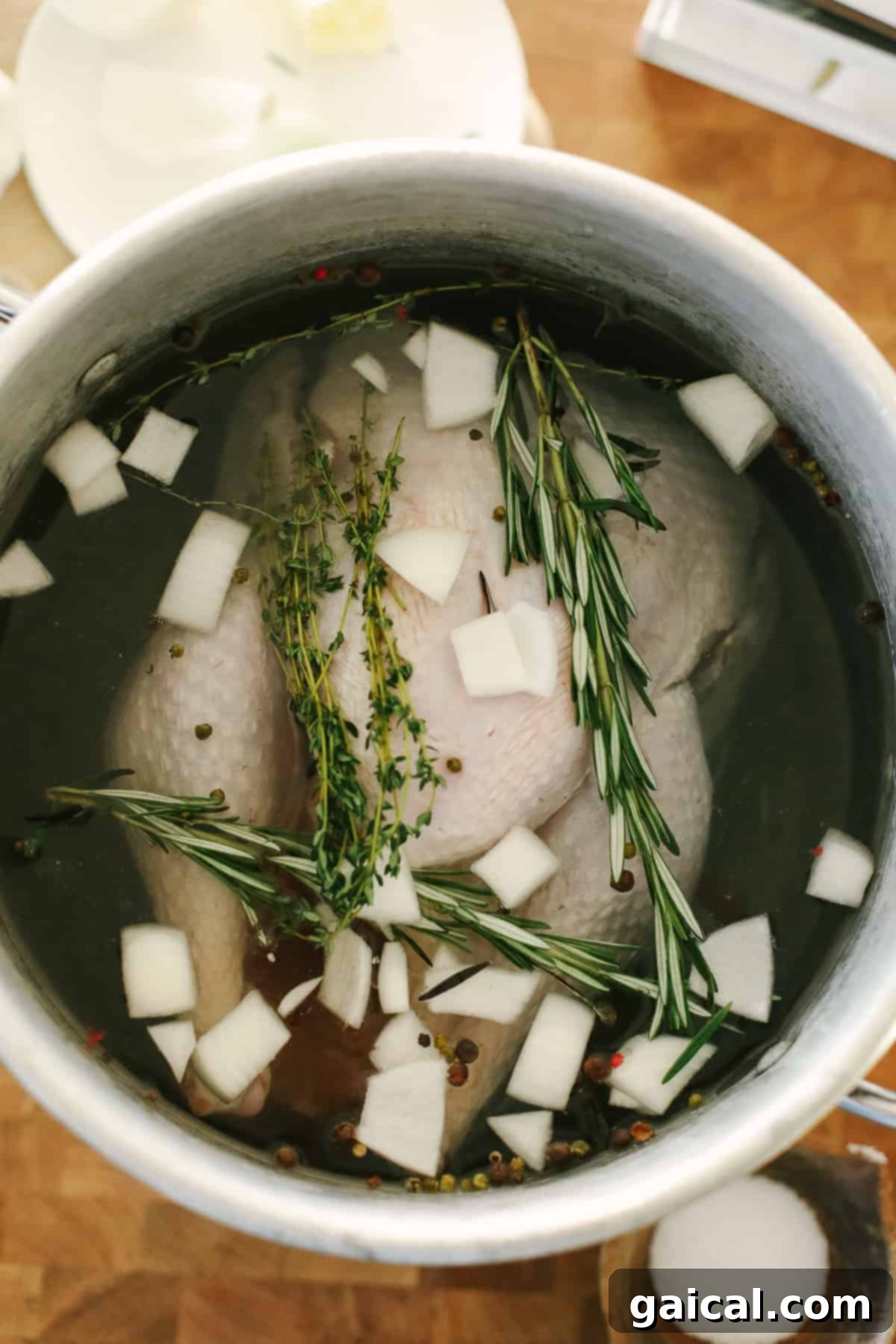 Ultimate Smoked Turkey Brine 10 A full turkey resting inside a large metal pot filled with brine and aromatic ingredients, ready for refrigeration.