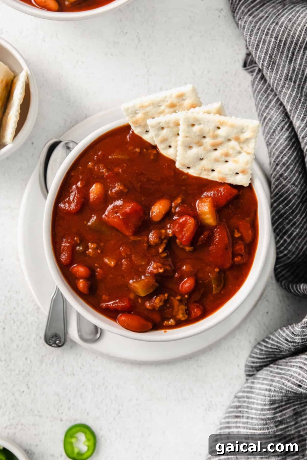 A bowl of rich Wendy's copycat chili, garnished with a generous sprinkle of shredded cheese and a dollop of sour cream, with crackers on the side.