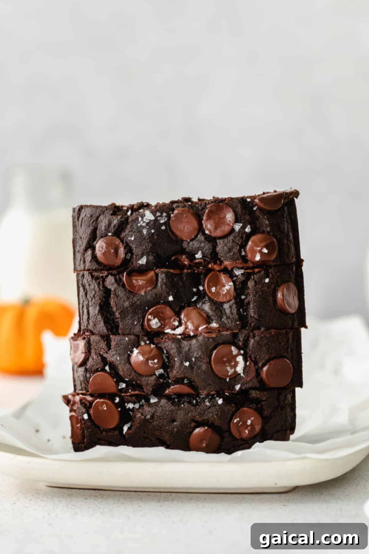 A stack of perfectly moist chocolate pumpkin bread slices, garnished with chocolate chips and a sprinkle of sea salt.