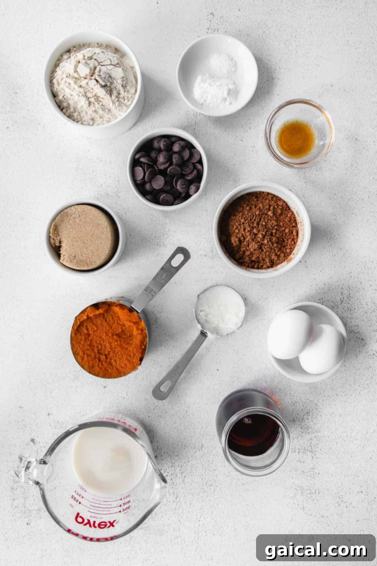 All the essential ingredients for baking chocolate pumpkin bread arranged in small bowls, including pumpkin puree, chocolate chips, and cocoa powder.