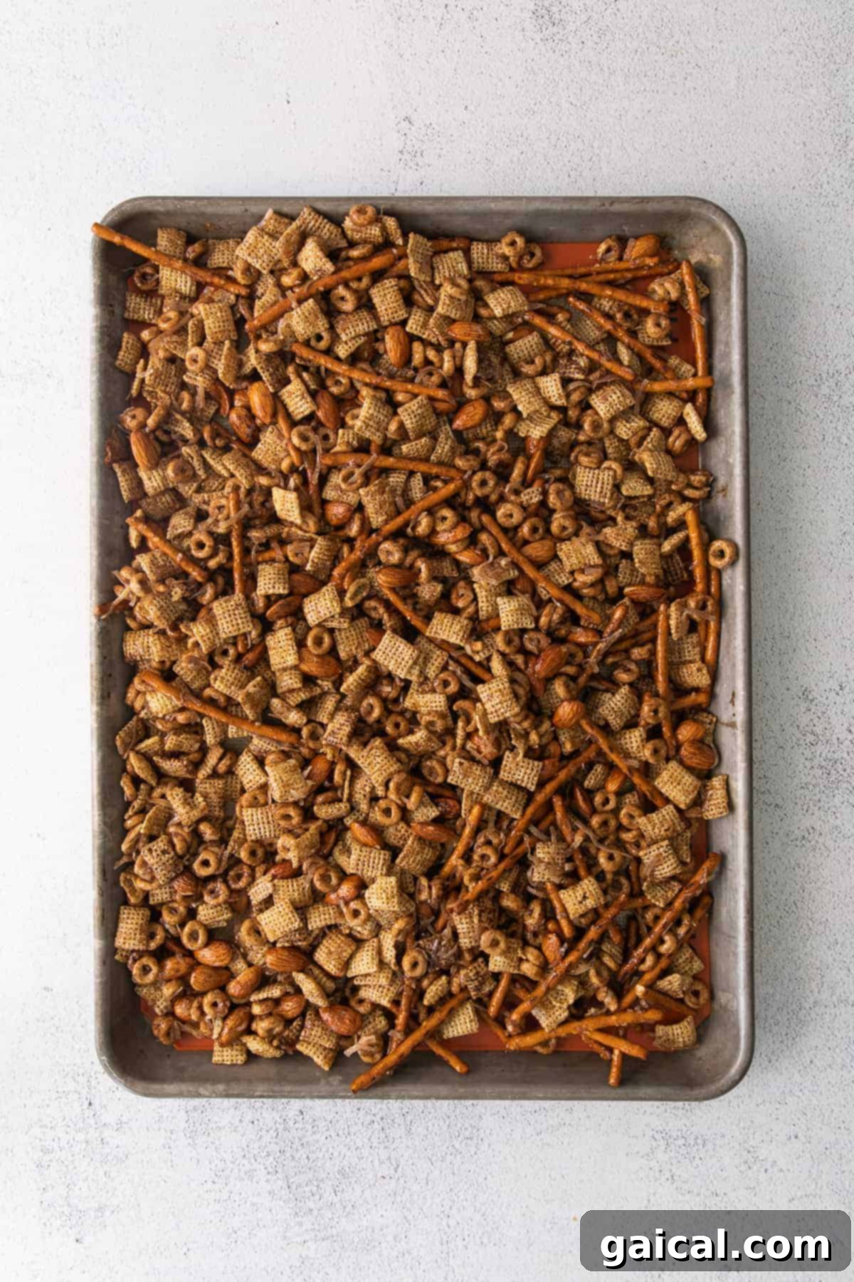 Maple Chai Chex Crunch 6 A fresh pan of golden-brown Chai Chex Mix, featuring a delightful mix of pretzels, Chex cereals, Cinnamon Cheerios, and almonds, cooling on parchment paper.