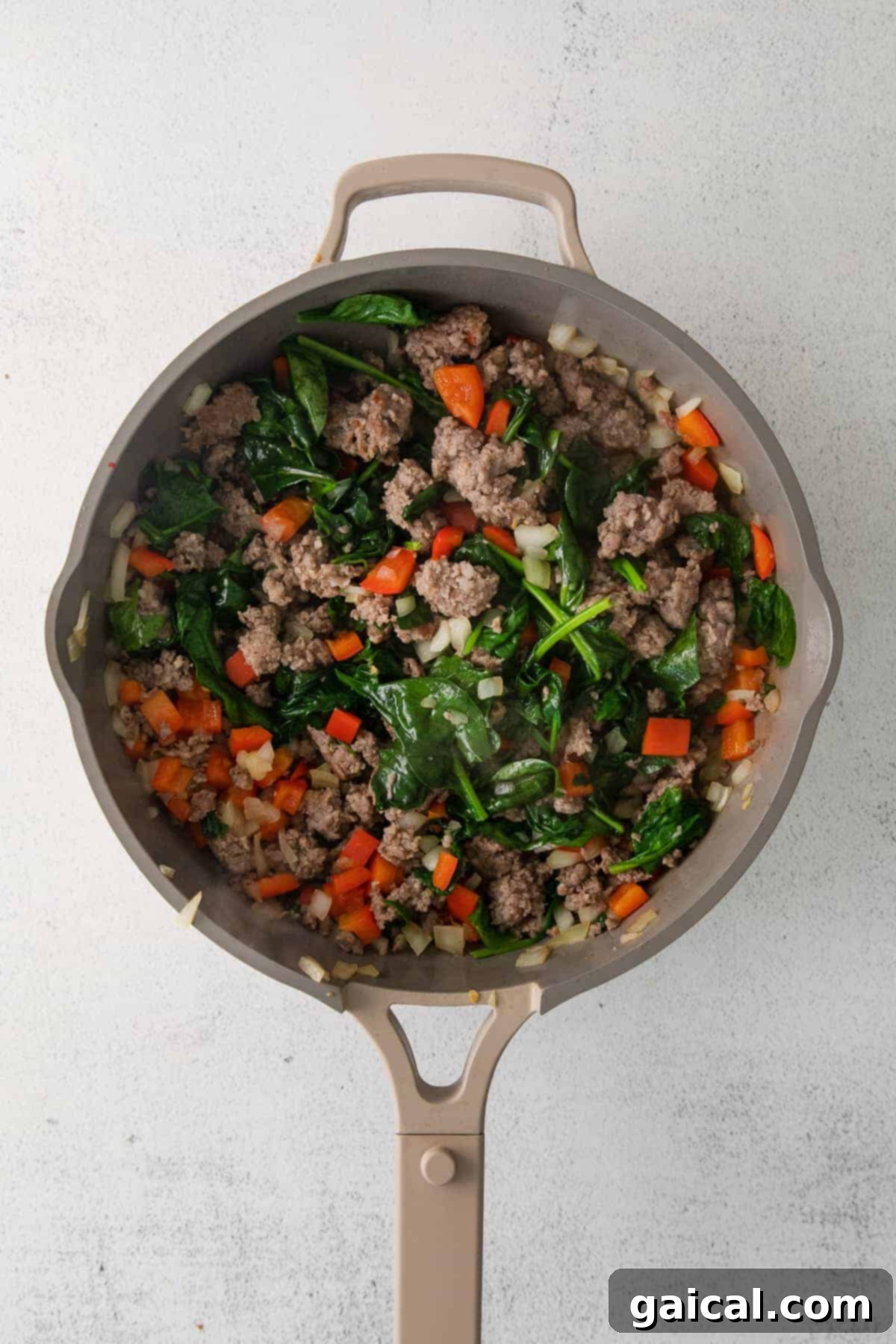 Hearty English Muffin Breakfast Casserole 3 Sausage, diced onion, bell peppers, and fresh spinach sautéing in a large skillet, releasing their aromas.