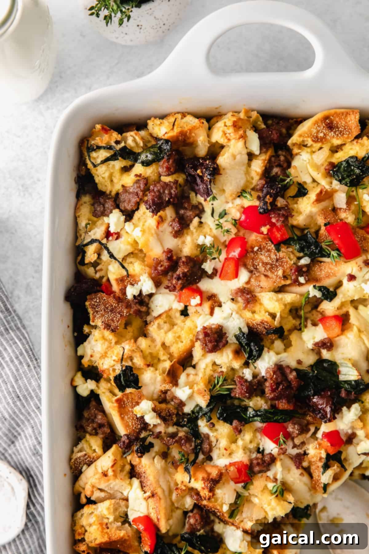 Hearty English Muffin Breakfast Casserole 5 A slice of English muffin breakfast bake, topped with vibrant fresh thyme and additional goat cheese crumbles, presented elegantly.