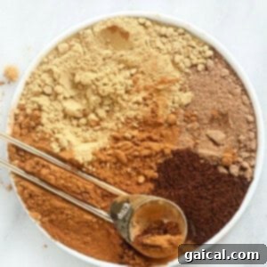 A crisp white bowl filled with a rich blend of ground spices, including cinnamon sticks, star anise, and whole cloves, all the ingredients for a homemade pumpkin pie spice blend.