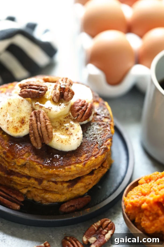 A beautifully plated stack of paleo pumpkin pancakes, artfully topped with sliced bananas and crunchy pecans, ready to be enjoyed as a wholesome and delicious breakfast.