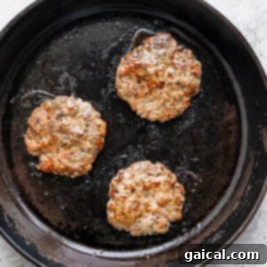 Breakfast sausage patties cooking in a skillet.