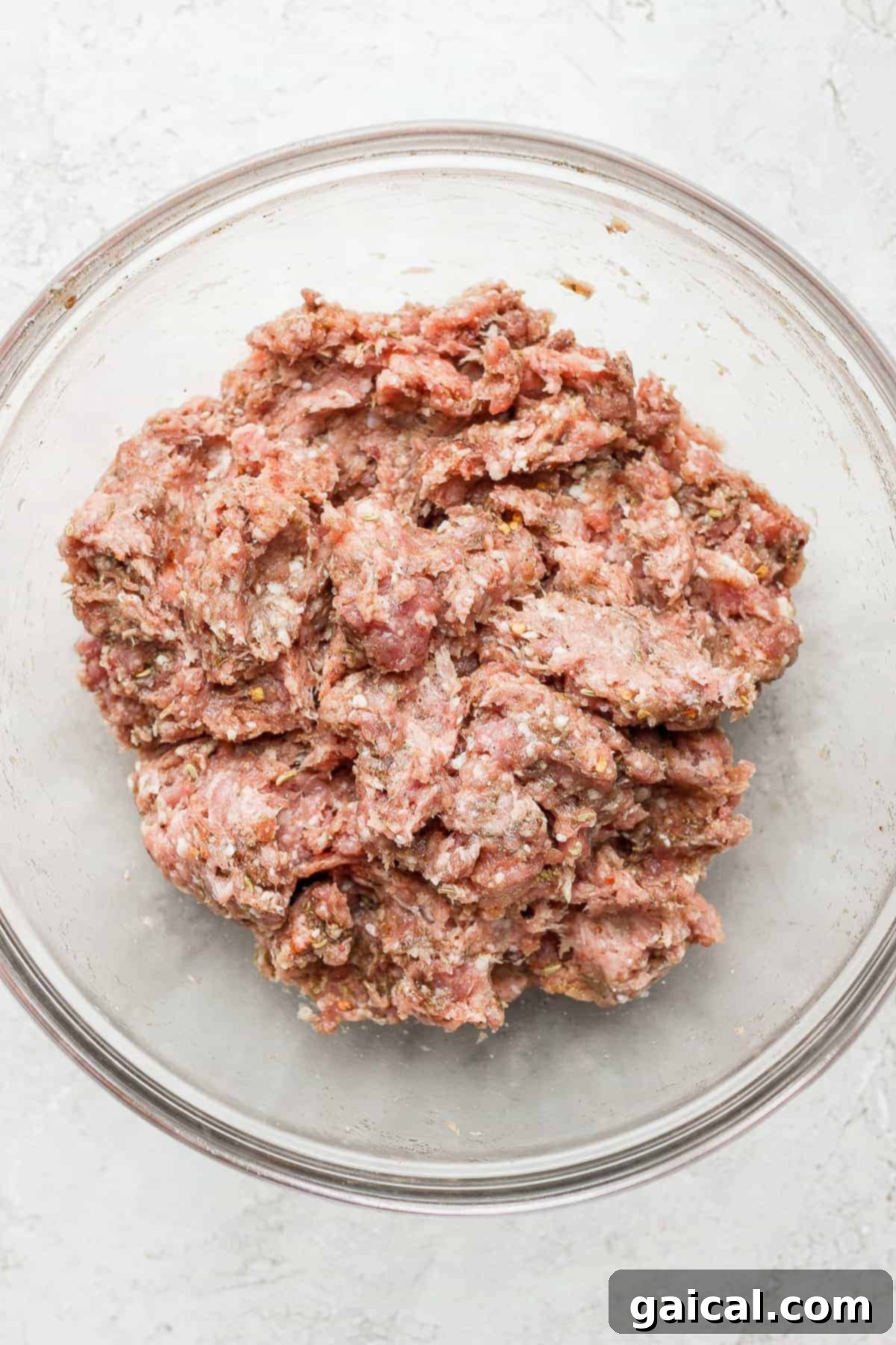 Mixed ground meat with seasoning in a bowl, ready to be formed into patties.