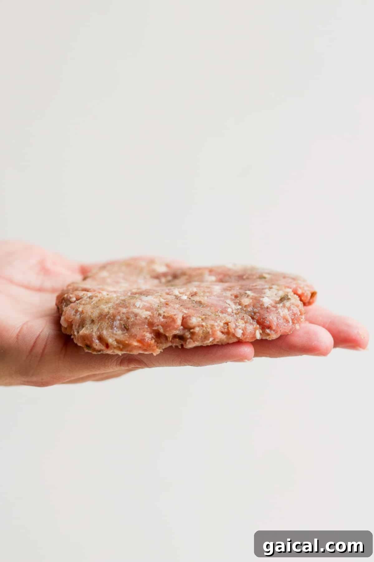 Homemade breakfast sausage patty in the palm of a hand, showing its ideal thinness.