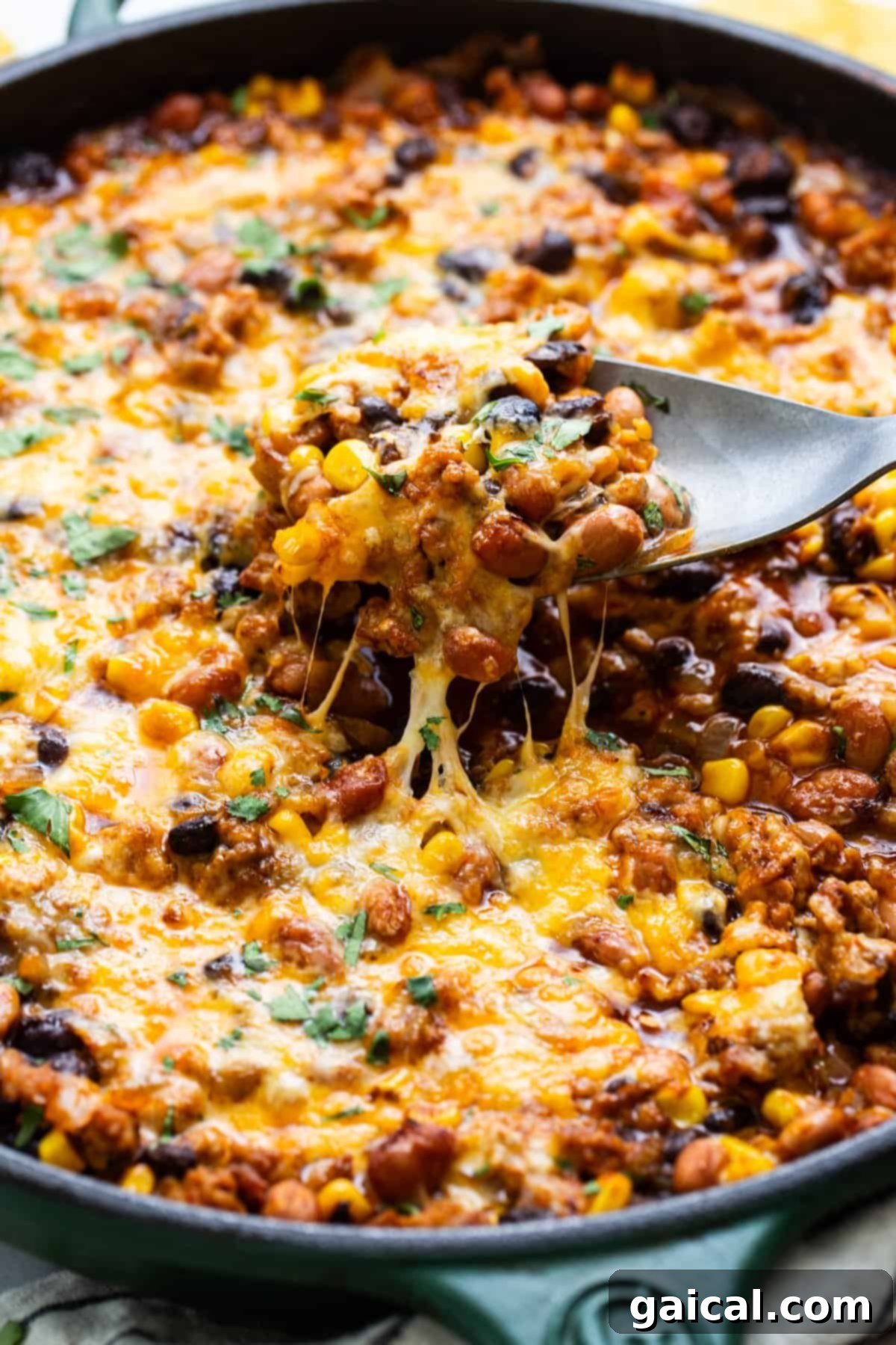 Vibrant Healthy Enchilada Dip 5 Skillet of baked cheesy chili with a spoon lifting a portion showing melted cheese stretch.
