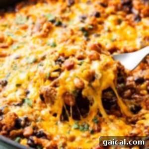 Vibrant Healthy Enchilada Dip 8 A skillet with melted cheese being lifted, revealing a cheesy, bean and meat mixture beneath.