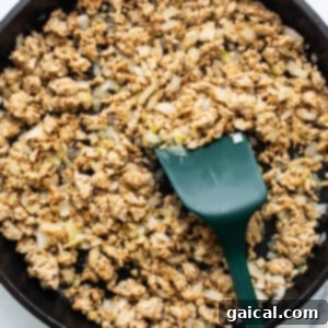 Vibrant Healthy Enchilada Dip 9 Ground meat cooked with diced onions in a cast iron skillet, with a green spatula.