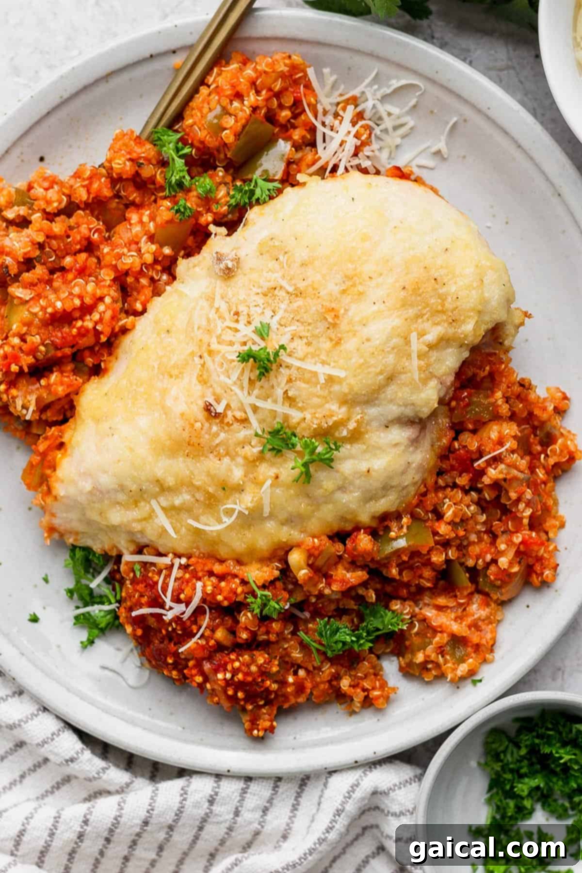 Parmesan Chicken Quinoa Bake 7 A perfectly cooked, tender slice of chicken breast resting atop a generous serving of vibrant tomato-infused quinoa, beautifully garnished with a sprinkle of fresh grated parmesan cheese and bright green parsley on a clean white plate, ready to be savored.