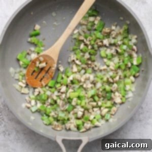 A pan filled with colorful diced green bell pepper, yellow onion, and mushrooms being expertly sautéed with a wooden spoon, releasing their fragrant aromas and softening to perfection.