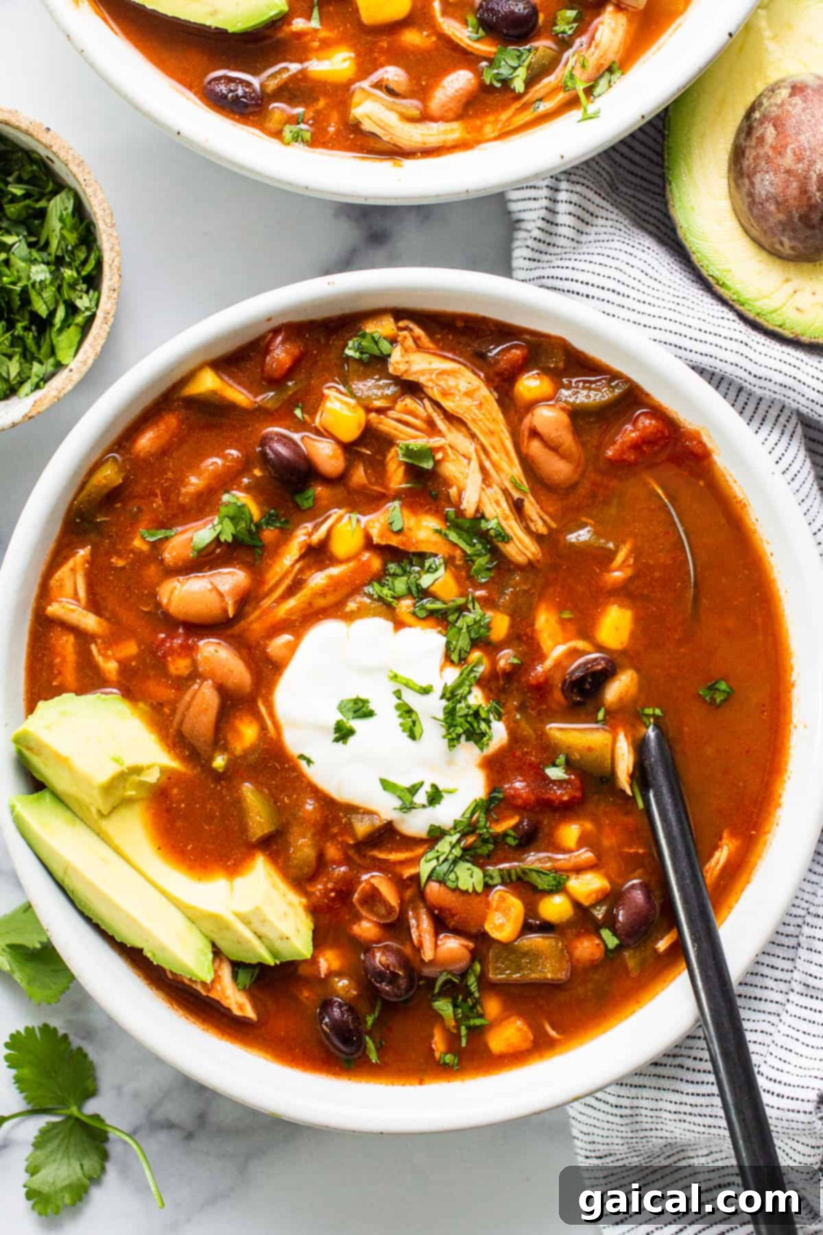 A vibrant bowl of crockpot chicken enchilada soup, garnished with fresh avocado slices and a dollop of sour cream.