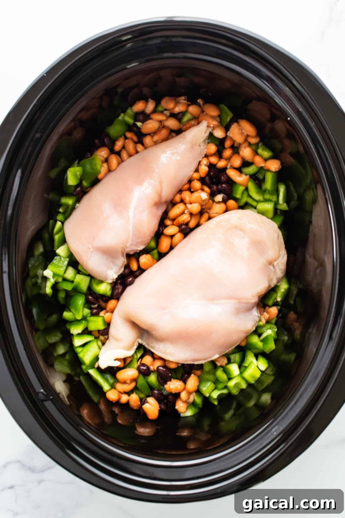 Close-up of the slow cooker filled with chicken, beans, bell peppers, and a rich, simmering enchilada sauce.
