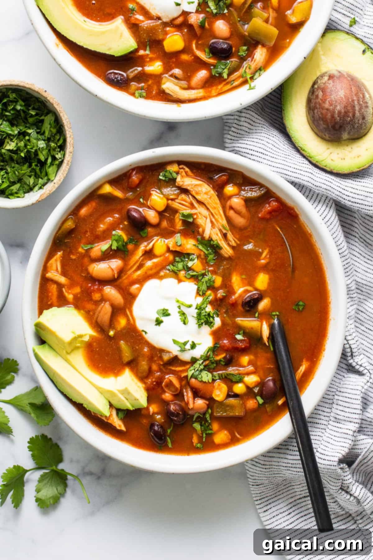 A close-up shot of a bowl of chicken enchilada soup with a spoonful being lifted, showcasing the rich texture and ingredients.
