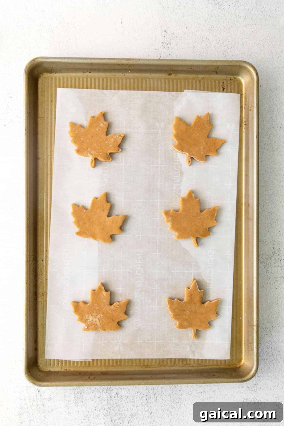 Cookie Cut-Outs on Baking Sheet Various holiday-shaped sugar cookie cut-outs neatly arranged on a parchment-lined baking sheet.
