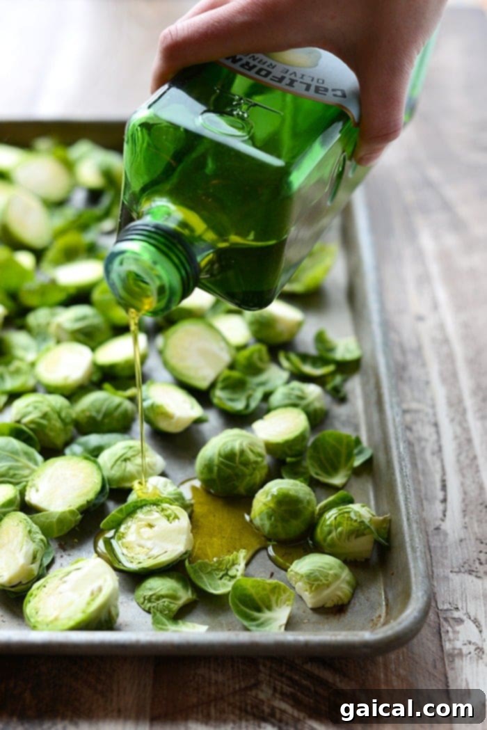 Fresh Brussels sprouts being generously drizzled with olive oil before roasting.