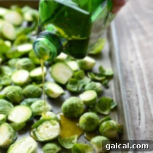 Brussels sprouts being drizzled with olive oil and balsamic vinegar for roasting.