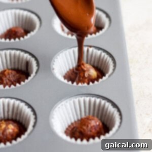 Salted Caramel Date Bites 7 A spoon carefully drizzles melted chocolate over date caramel balls nestled in a muffin tin, creating the top layer of the cups.