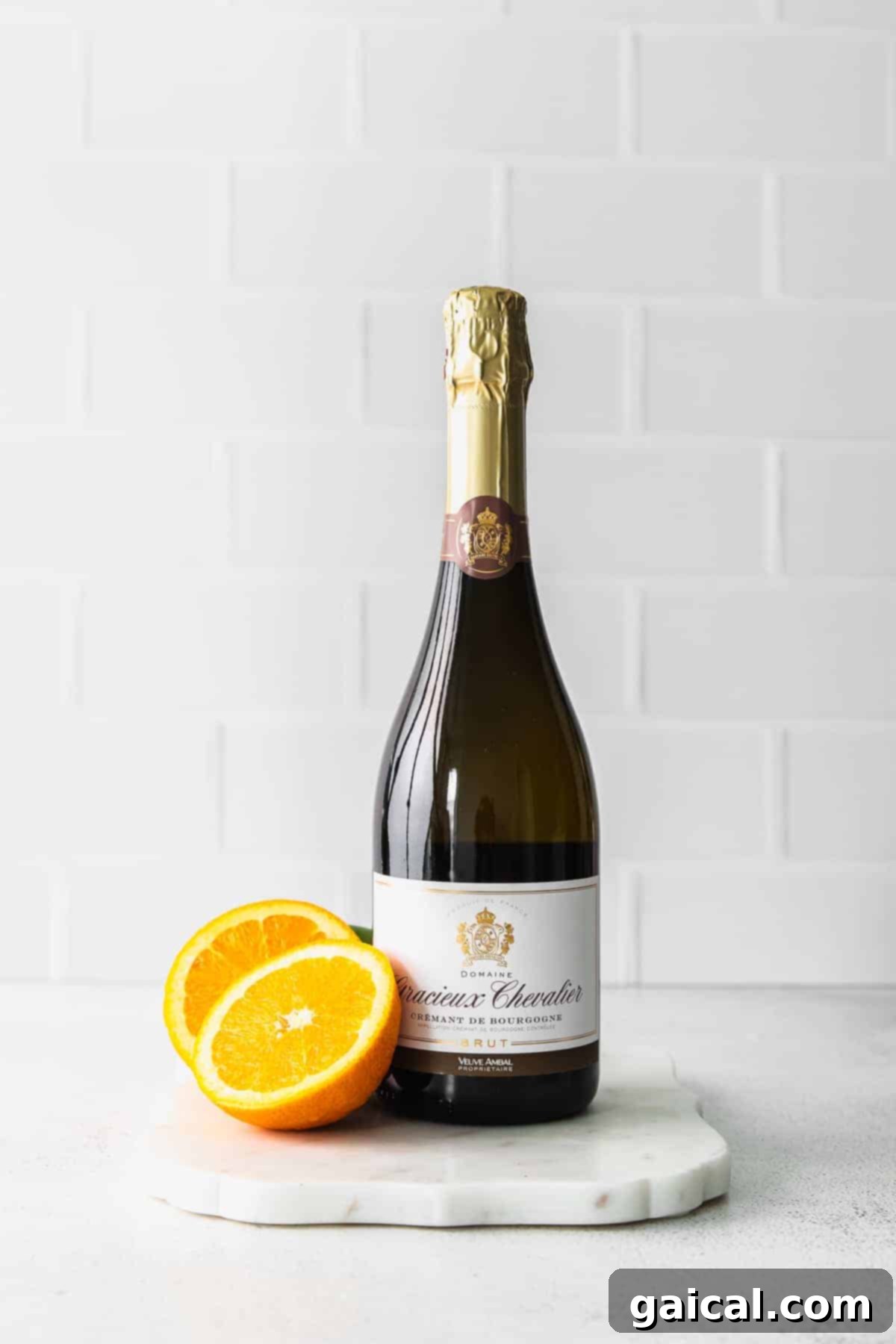 Champagne and Orange Juice for Mimosas A pristine bottle of sparkling wine stands beside a bowl of vibrant orange slices and a pitcher of fresh orange juice, highlighting the simple ingredients for a classic mimosa.