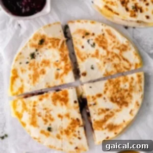Leftover Thanksgiving turkey quesadilla topped with cranberry chutney on a white plate, sliced into wedges.
