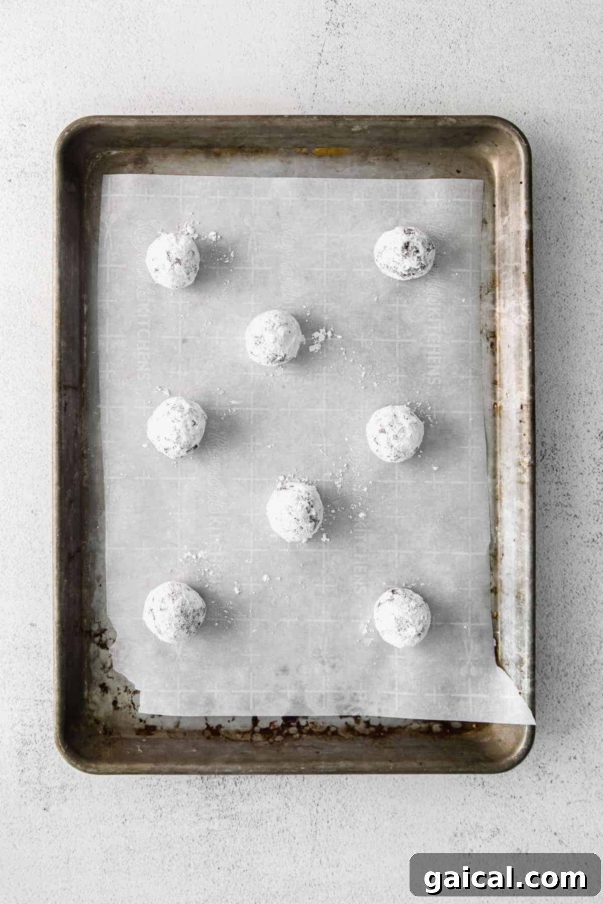 Dough Balls Ready for Their Transformation Chocolate Crinkle Cookie dough balls, generously coated in powdered sugar, arranged on a parchment-lined baking sheet.